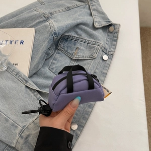 Detail of purple canvas mini pouch with black spring hook and woven strap on denim jacket