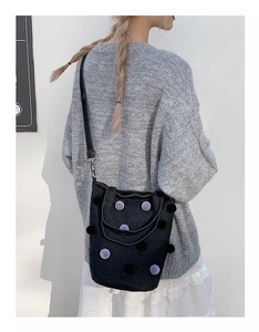 Detail view of a black denim bucket bag featuring plush polka dots and a leather strap