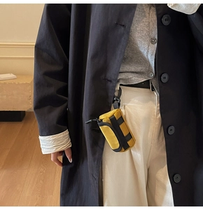 Detailansicht der gelben Mini-Canvas-Tasche als Accessoire an einem schwarzen Mantel