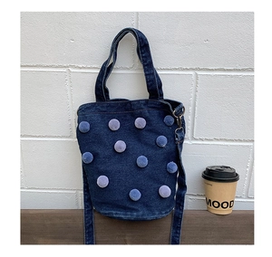 Detail of dark blue denim bucket bag with soft light blue pom-poms and metal hardware