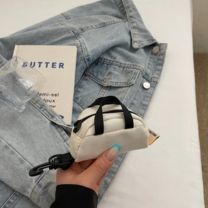 Mini white canvas coin purse with black straps and carabiner held in hand by a model