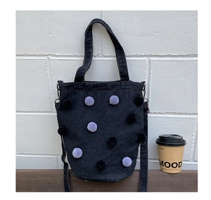 Close-up of a blue denim bucket bag featuring purple and black plush pom-poms on wood