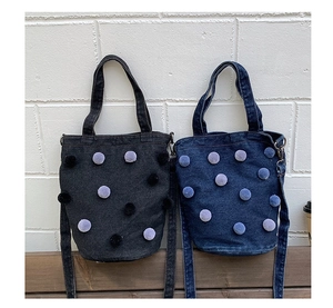 Detailed view of denim tote bags with colorful fur pompom charms on a wooden bench