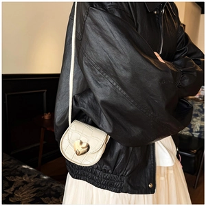 Détail du mini sac crème à motif pierre avec fermoir cœur doré sur une veste en cuir