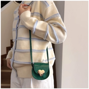 Détail d'un mini sac bandoulière vert cœur avec texture crocodile porté par un mannequin