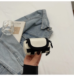Nahaufnahme der cremefarbenen Mini-Schlüsseltasche mit schwarzem Rand an einer Jeansjacke