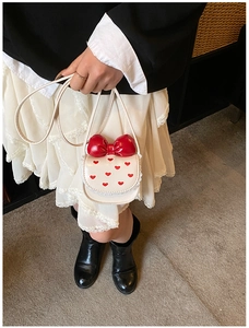 Détail du mini sac blanc avec grand nœud rouge, broderie cœur et bordure en dentelle