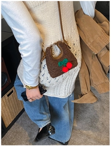 Close-up of brown plush mini cherry bag on a model featuring soft faux fur and red poms