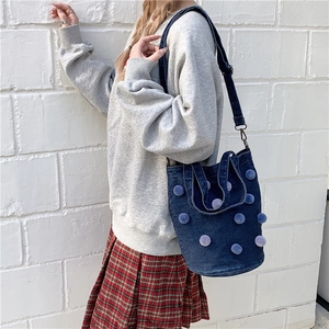 Deep blue denim tote bag with light blue pom-poms and adjustable strap on a female model