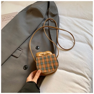 Close-up of a mini plaid crossbody bag with a brown bow on a gray blazer backdrop