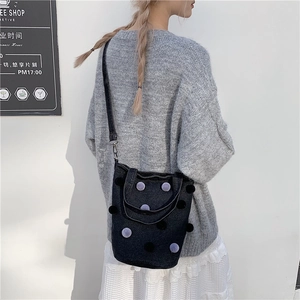 Chic black denim bucket bag with purple pom-poms shown on a model in a lifestyle setting