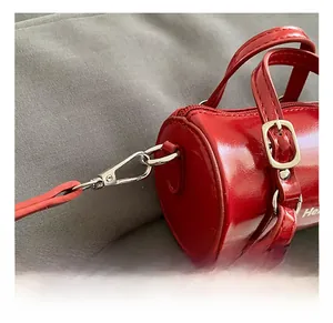 Détail du sac cylindre rouge montrant la finition brillante et le crochet en métal