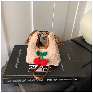 Close-up of plush beige mini bag with crochet cherry detail on top of a book
