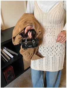 Détail d'un sac cylindre en cuir verni noir avec boucle en métal sur une tenue décontractée