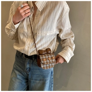 Detail of checkered mini crossbody bag with leather bow and floral accents on vintage shirt
