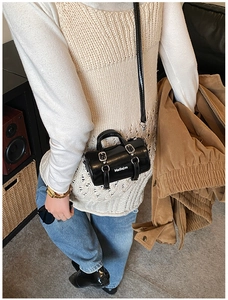 Détail d'un sac cylindrique noir brillant avec bandoulière réglable et fini laqué