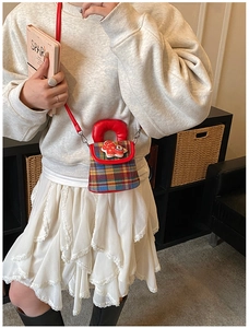Détail du mini sac à carreaux avec patch cheval rouge et poignée porté par un modèle