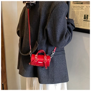 Vue détaillée du sac cylindre en cuir verni rouge avec bandoulière et boucle en métal