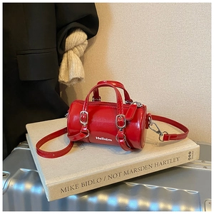 Détail d'un sac cylindrique rouge en cuir verni avec bandoulière réglable sur un livre