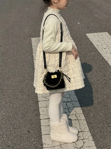 Close-up of black quilted mini bucket bag for kids with gold chain and twist lock detail