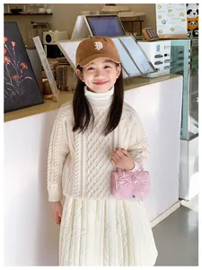 Detail of child wearing ivory cable knit sweater and pink bow handbag in a cozy cafe