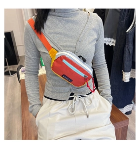 Detail of multi-color crossbody chest bag with adjustable strap and red zipper puller