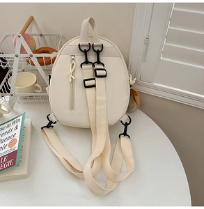 Detail view of cream canvas backpack with adjustable straps and vertical front zipper