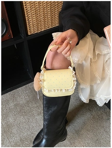 Détail d'un mini sac jaune à pois avec bordure en dentelle et breloque cœur en peluche