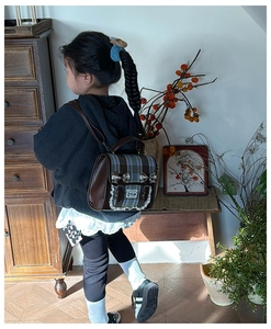 Detail of vintage plaid kids backpack featuring bow accents and brown leather trim