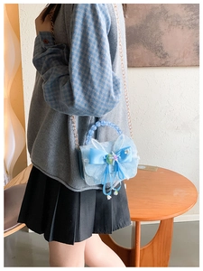 Detail of light blue girls' bag with white lace, silk bow, and beaded handle strap