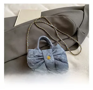 Detail of blue denim crossbody bag with bow design, diamond quilting and gold floral clasp