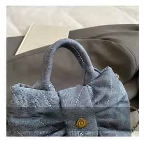 Close-up of blue denim quilted handbag featuring bow design and golden flower clasp