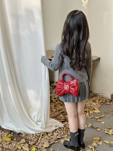 Detail of red bow-shaped quilted crossbody bag with gold flower clasp and metal chain