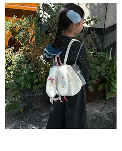 Outdoor shot of a child wearing the white plush bunny backpack with red checkered bows