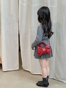 Detail of red bow-shaped quilted crossbody bag with golden flower clasp worn by a child
