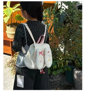 Detail of white plush bunny ears with red plaid bow and heart embroidery on backpack