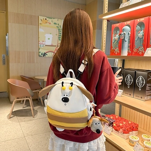 Cute white and yellow dog-themed backpack with ears and plush pendant worn by a woman