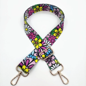 Close-up of floral print bag strap with golden metal hooks on white background