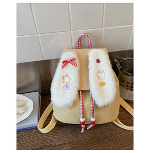 Detail of yellow corduroy backpack featuring large plush bunny ears and cartoon badges