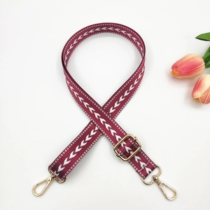 Détail de la bandoulière en nylon bordeaux de 2,5 cm avec motif flèche et boucles dorées