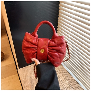 Detail of red quilted bow-shaped handbag with gold flower clasp and chain strap