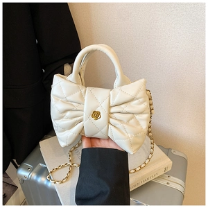 Detailed close-up of white quilted bow bag with golden camellia clasp and chain strap