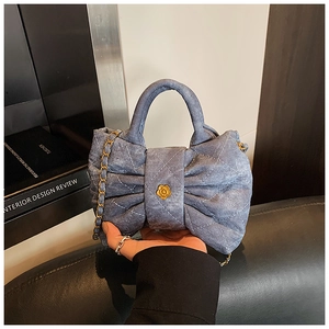 Detail of blue denim bow purse with white quilted stitching and golden floral buckle