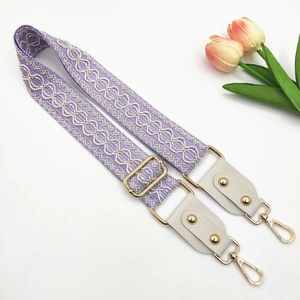 Close-up of adjustable purple woven bag strap with white geometric pattern and gold hardware