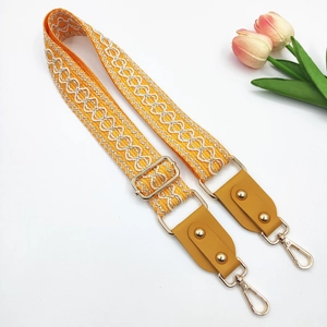Detail of adjustable orange embroidered bag strap with geometric waves and gold metal clips