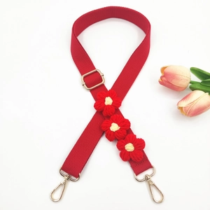 Close-up of red woven shoulder strap with handmade floral accents and gold metal hooks