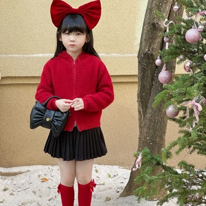 Girl in red faux fur hoodie and black quilted bow bag by a Christmas tree