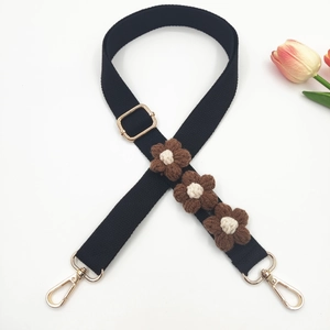 Detail of black woven shoulder strap with handcrafted floral accents and gold metal hooks