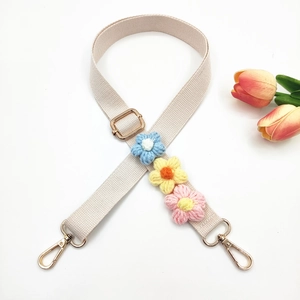 Detail of beige woven bag strap with colorful knitted flowers and gold metal hardware