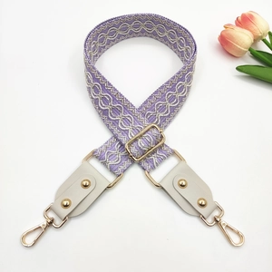 Close-up of lilac woven bag strap with white geometric embroidery and gold rivets